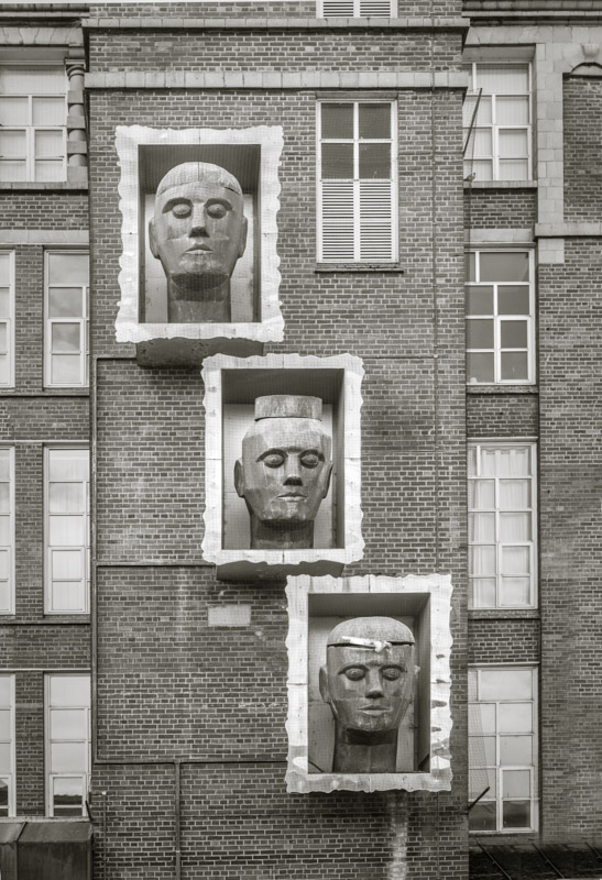 A sculpture of three heads on a mill wall